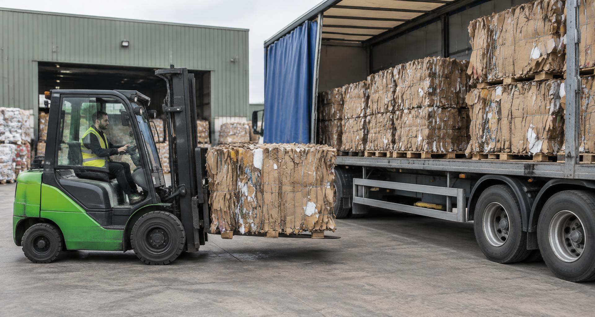 Forklift loading strapped cardboard bales onto a trailer for collection